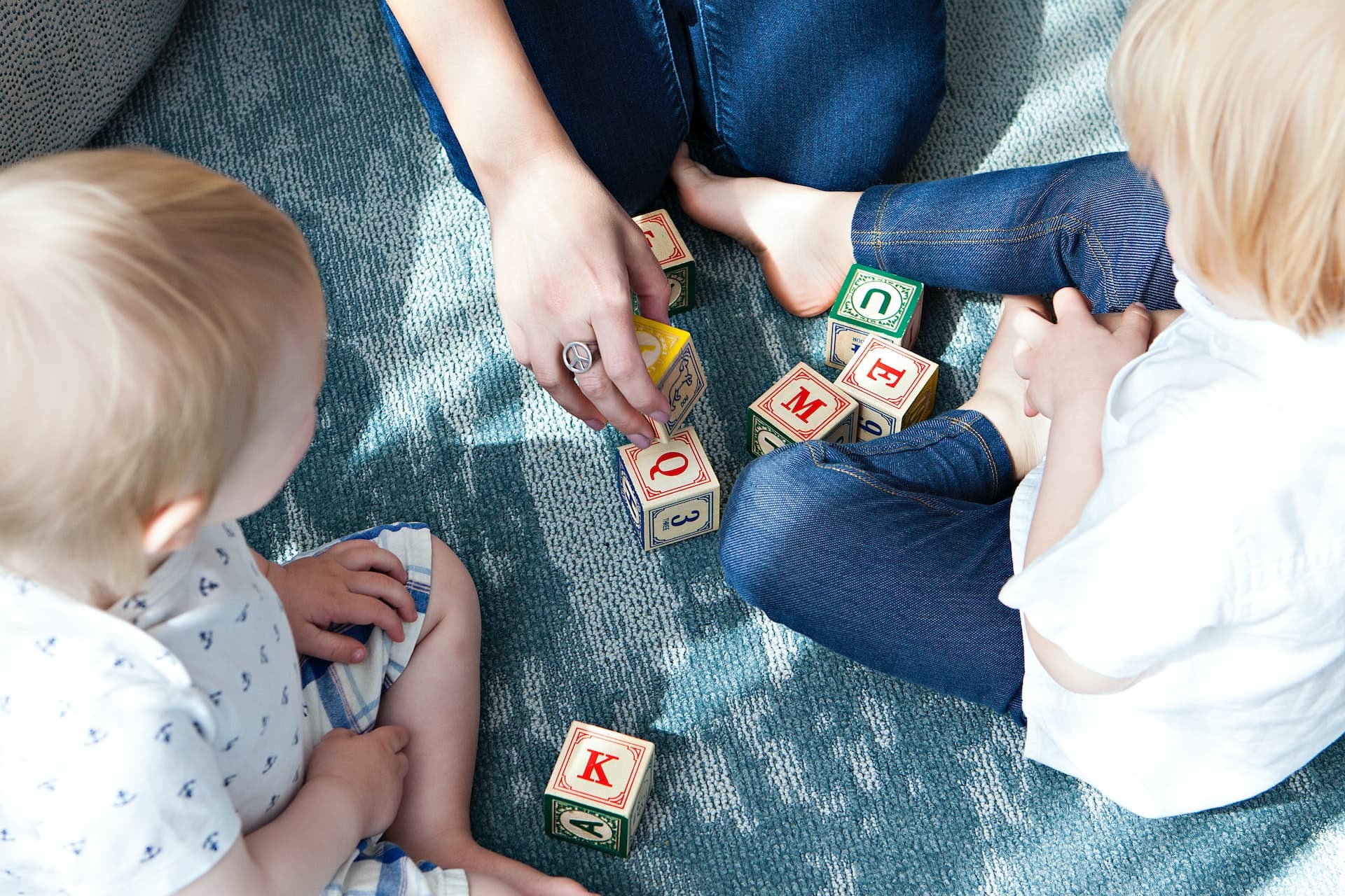 Toddlers playing with alphabet blocks beside an educator